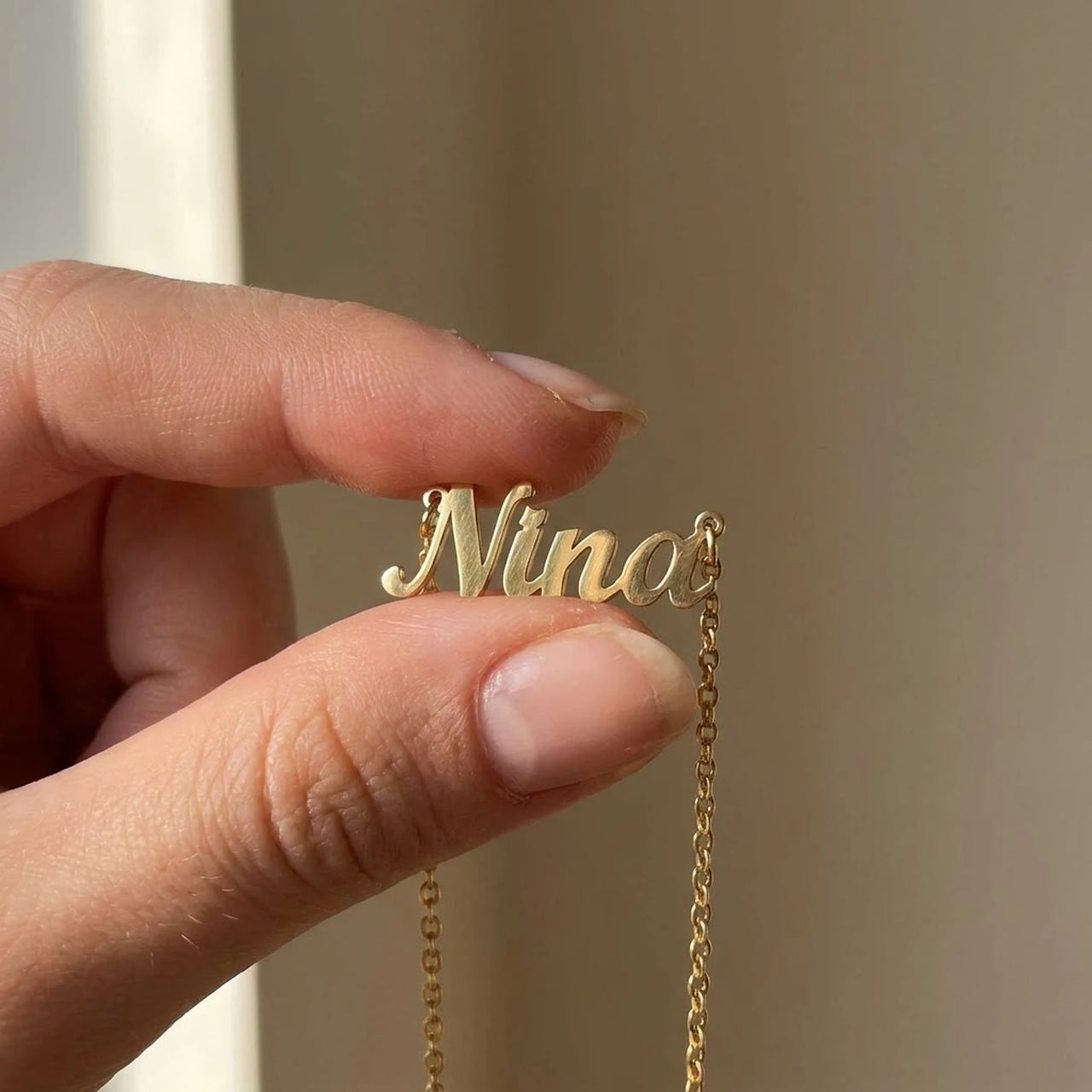 Minimalist Name Necklace pendant held between two fingertips showing its true size, the name Nina | SKU: minimalistnn-gold