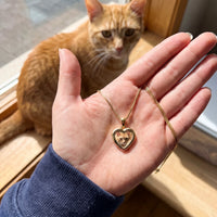 Thumbnail for Customer photo: the gold heart photo necklace with her cat's photo, her cat in the background | SKU: TPH-CHTN-GOLD-SMALL