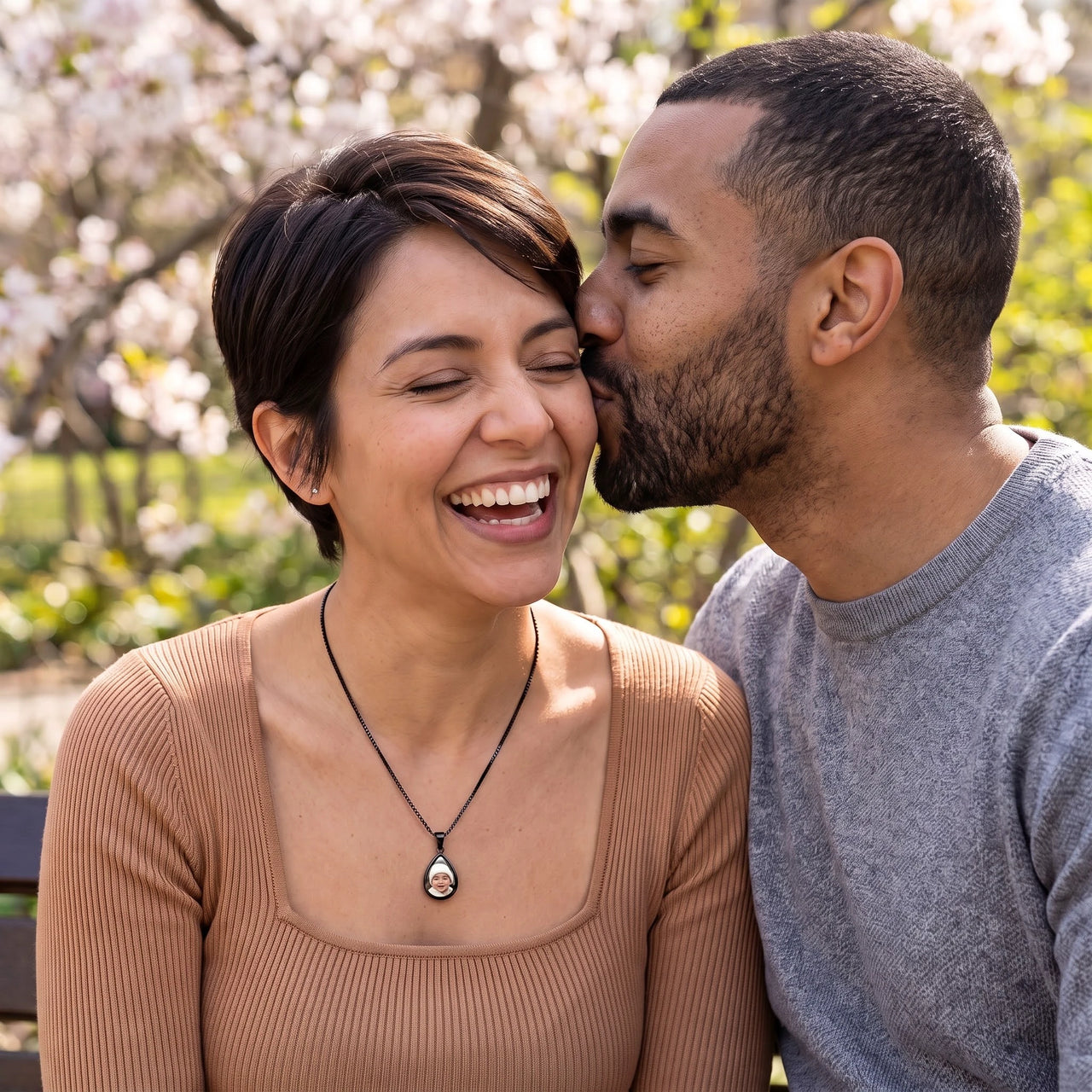 Couple laughing under spring blossoms, she wears the black secret drop photo necklace | SKU: TPH-DRPN-BLACK