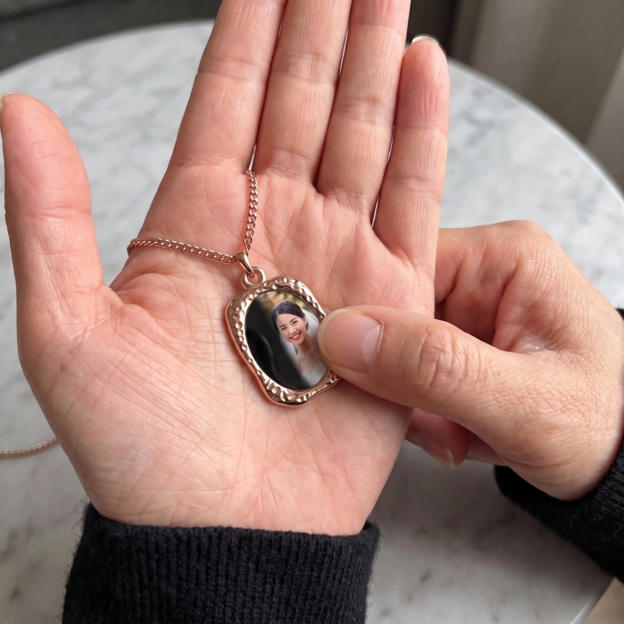 Thumb warming the rose gold oval pendant: the hidden photo appears under the thumb while the rest stays black | SKU: TPH-OVLN-ROSEGOLD